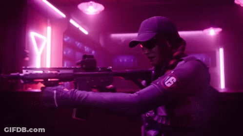 A Man Is Holding A Rifle In A Dark Room With Neon Lights . GIF