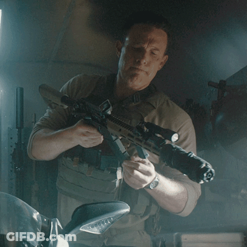 A Man Is Holding A Rifle With A Scope That Has The Letter O On It GIF