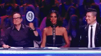 A Man Is Holding A Sign With The Number 9 On It While A Woman Looks On . GIF