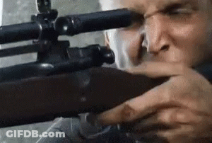A Man Is Holding A Sniper Rifle In His Hand And Looking Through The Scope . GIF