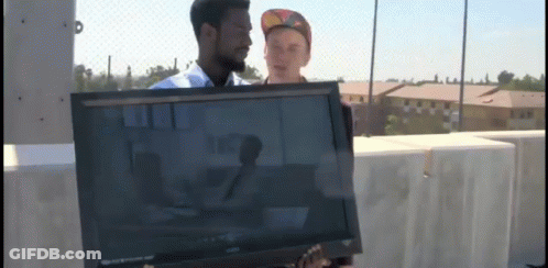 A Man Is Holding A Sony Television While Another Man Stands Behind Him GIF