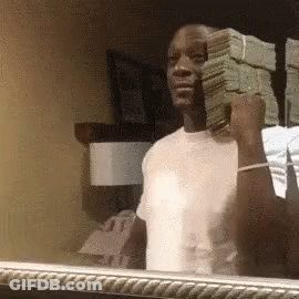 A Man Is Holding A Stack Of Money In His Hand In Front Of A Mirror . GIF