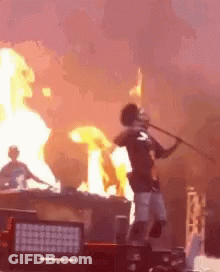 A Man Is Holding A Stick In Front Of A Fire While Standing On A Stage . GIF
