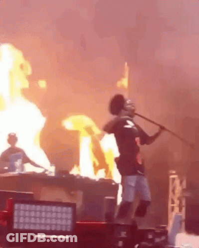 A Man Is Holding A Stick In Front Of A Fire While Standing On A Stage . GIF