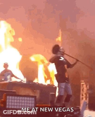 A Man Is Holding A Stick In Front Of A Fire With The Words Me At New Vegas Written On The Bottom GIF