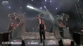 A Man Is Holding A Sword In Front Of A Monster Logo On A Stage GIF