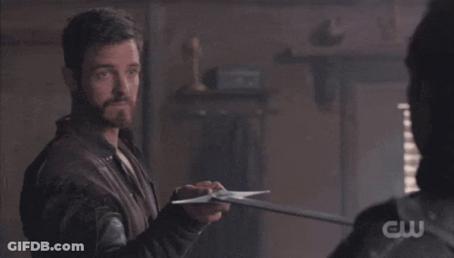 A Man Is Holding A Sword In Front Of Another Man With A Cw Logo Visible GIF