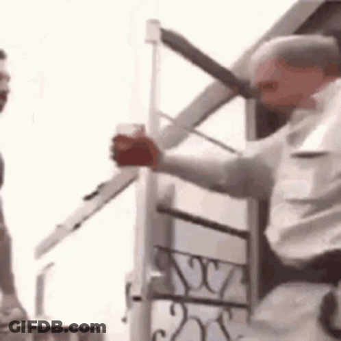 A Man Is Holding A Sword In His Hand While Standing Next To A Building . GIF