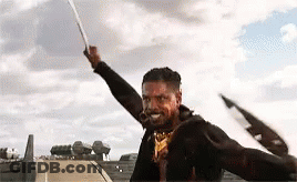 A Man Is Holding A Sword In The Air In A Field . GIF
