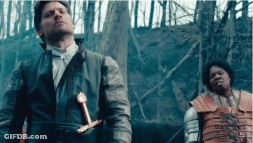 A Man Is Holding A Sword While Standing Next To Another Man . GIF