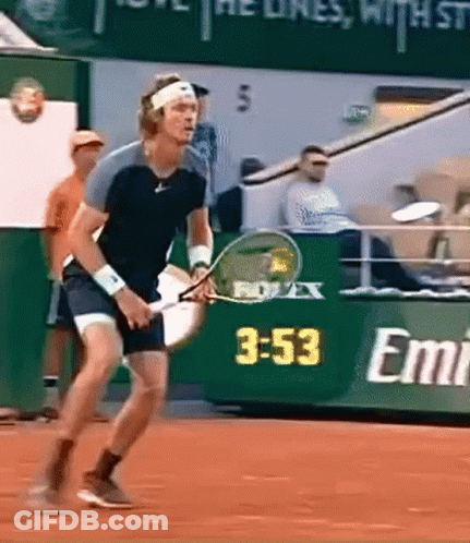 A Man Is Holding A Tennis Racket In Front Of A Sign That Says Emirates GIF
