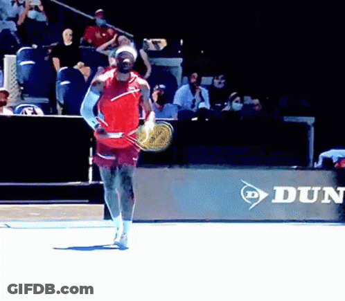 A Man Is Holding A Tennis Racquet In Front Of A Dunlop Ad GIF