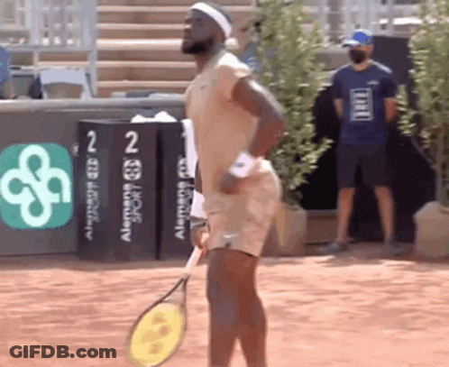 A Man Is Holding A Tennis Racquet In Front Of A Sign That Says ' Alemania Sport ' On It GIF