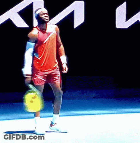 A Man Is Holding A Tennis Racquet In Front Of A Sign That Says Km GIF