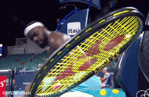 A Man Is Holding A Tennis Racquet In Front Of An Itau Banner GIF