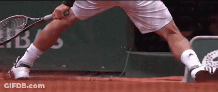 A Man Is Holding A Tennis Racquet On A Red Court GIF