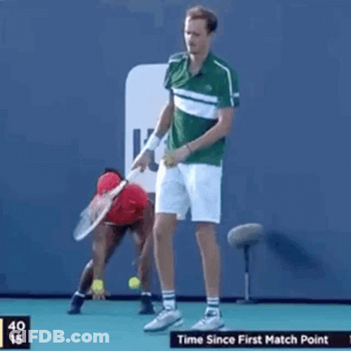 A Man Is Holding A Tennis Racquet On A Tennis Court While A Woman Stands Behind Him . GIF