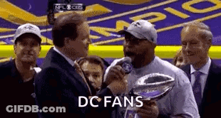 A Man Is Holding A Trophy And Talking Into A Microphone In Front Of A Crowd . GIF