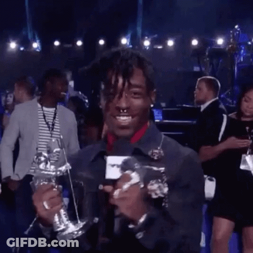 A Man Is Holding A Trophy And Talking Into A Microphone While Standing On A Stage . GIF