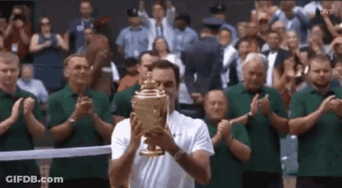 A Man Is Holding A Trophy In Front Of A Crowd Of People Applauding . GIF