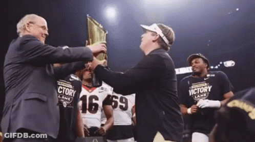 A Man Is Holding A Trophy In Front Of A Group Of Football Players Wearing Victory Lane Shirts GIF