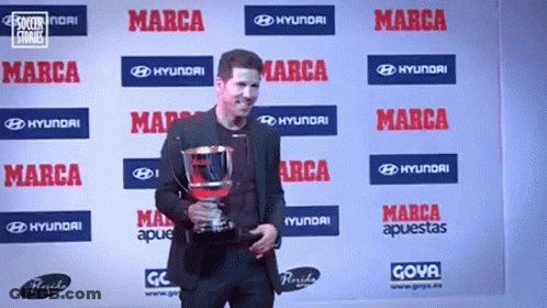 A Man Is Holding A Trophy In Front Of A Wall That Says Marca On It GIF