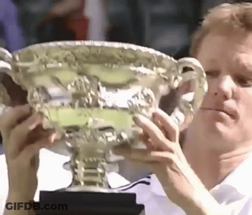 A Man Is Holding A Trophy In His Hands And Looking At It . GIF