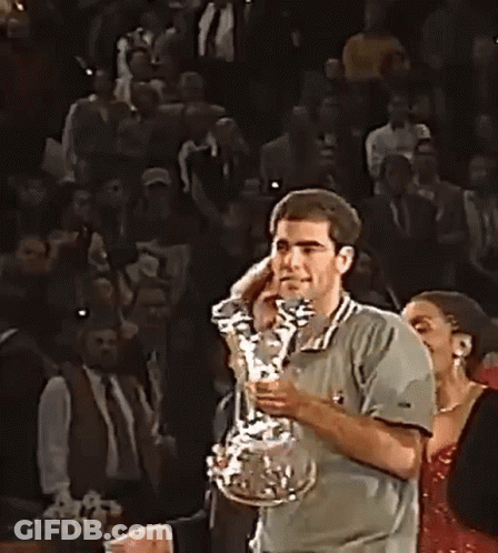 A Man Is Holding A Trophy In His Hands In Front Of A Crowd Of People . GIF