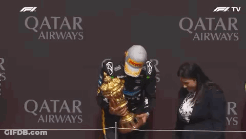 A Man Is Holding A Trophy On A Stage In Front Of A Qatar Airways Sign . GIF