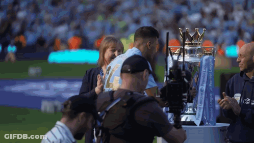 A Man Is Holding A Trophy That Says Premier League On It GIF