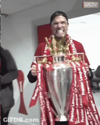 A Man Is Holding A Trophy With Red Ribbons Around It And Making A Funny Face . GIF