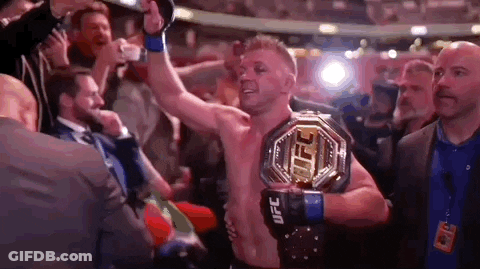A Man Is Holding A Ufc Heavyweight Championship Belt In A Boxing Ring . GIF