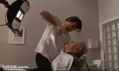 A Man Is Holding A Woman In A Dental Chair While A Dentist Cuts Her Teeth . GIF