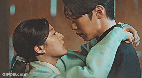 A Man Is Holding A Woman In His Arms And Kissing Her . GIF