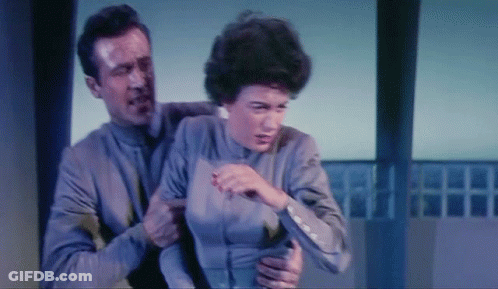 A Man Is Holding A Woman In His Arms And She Is Looking At Him GIF