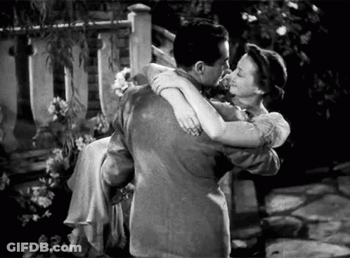 A Man Is Holding A Woman In His Arms And They Are Kissing . GIF