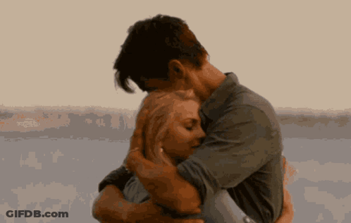 A Man Is Holding A Woman In His Arms In Front Of A Body Of Water . GIF