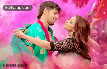 A Man Is Holding A Woman In His Arms While They Are Dancing In A Pink Room . GIF