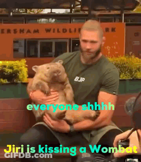 A Man Is Holding A Wombat In Front Of A Sign That Says ' Everyone Shhhh ' GIF
