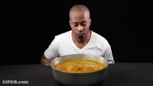 A Man Is Holding A Wooden Spoon In Front Of A Pot Of Soup GIF
