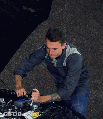 A Man Is Holding A Wrench In Front Of A Car With The Hood Open GIF