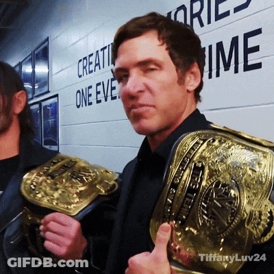 A Man Is Holding A Wrestling Belt In Front Of A Wall That Says " Create One Eve " GIF