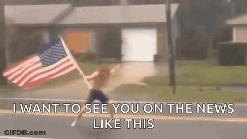 A Man Is Holding An American Flag On The Side Of The Road . GIF