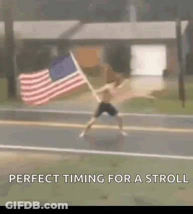 A Man Is Holding An American Flag On The Side Of The Road . GIF