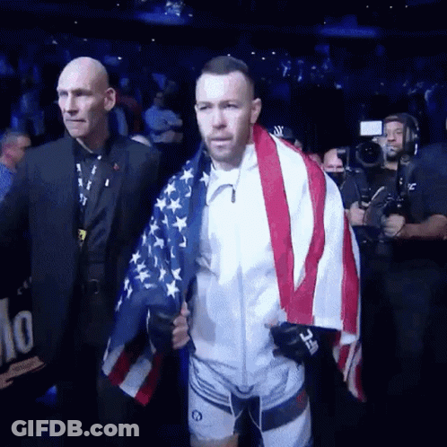 A Man Is Holding An American Flag While Walking Through A Stadium . GIF