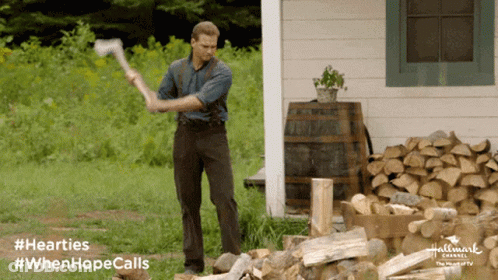 A Man Is Holding An Axe In Front Of A Pile Of Logs And A Sign That Says Hallmark Channel GIF
