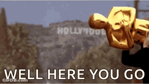 A Man Is Holding An Oscar Statue In Front Of A Sign That Says Hollywood GIF