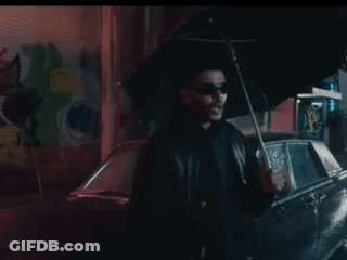 A Man Is Holding An Umbrella In Front Of A Car . GIF