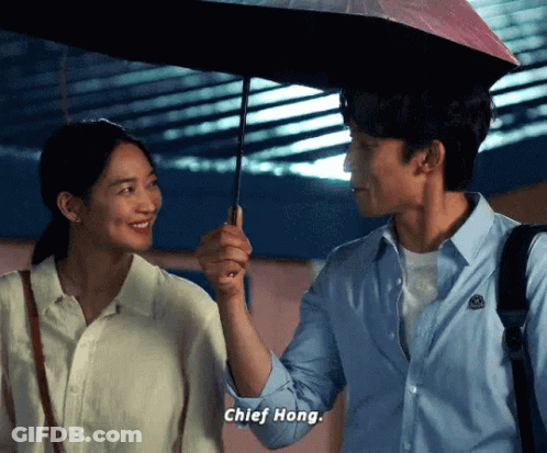 A Man Is Holding An Umbrella Over A Woman 'S Head And They Are Looking At Each Other . GIF