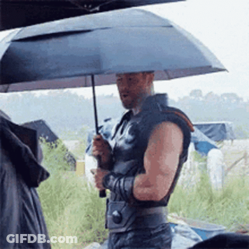 A Man Is Holding An Umbrella While Standing In The Rain GIF